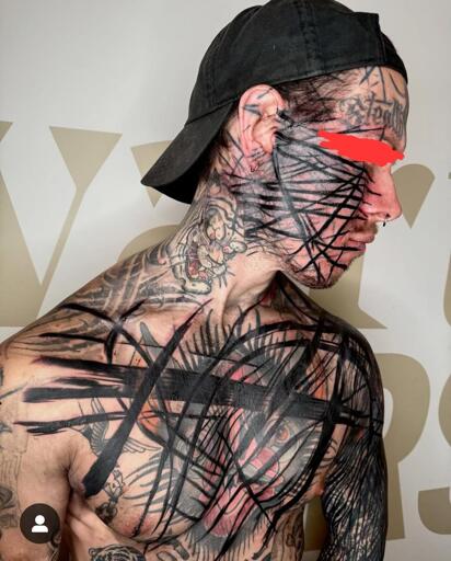 A heavily tattooed man wearing a black cap is shown in a side profile. His face, neck, and upper body are covered in intricate black linework and abstract tattoo patterns, layered over older tattoos. His eyes are redacted with a red mark. The background features a white wall with large, partially visible gold letters.