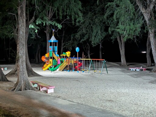 A kids playground at night, lit up by bright lights at the beach.